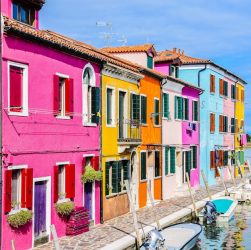 Vibrant multi-colored houses line a canal in Burano, Italy during summer.