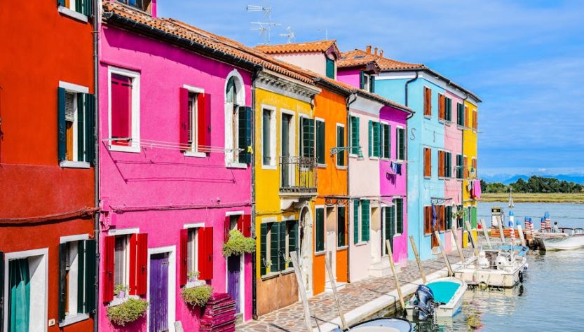 Vibrant multi-colored houses line a canal in Burano, Italy during summer.