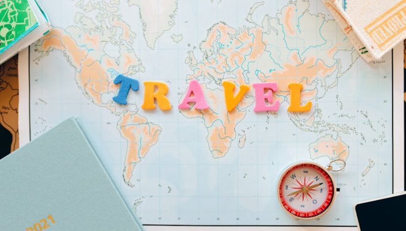 Flat lay of a map with colorful letters "TRAVEL" and a compass for planning adventures.