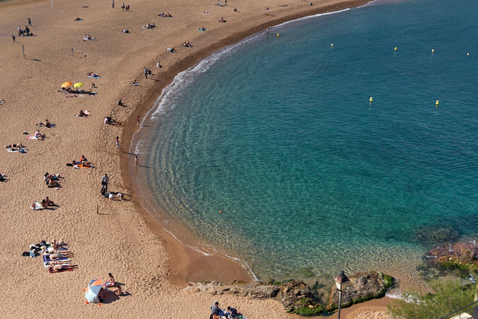 A stunning aerial view of a sandy beach in Barcelona, Spain, with sunbathers and turquoise waters.