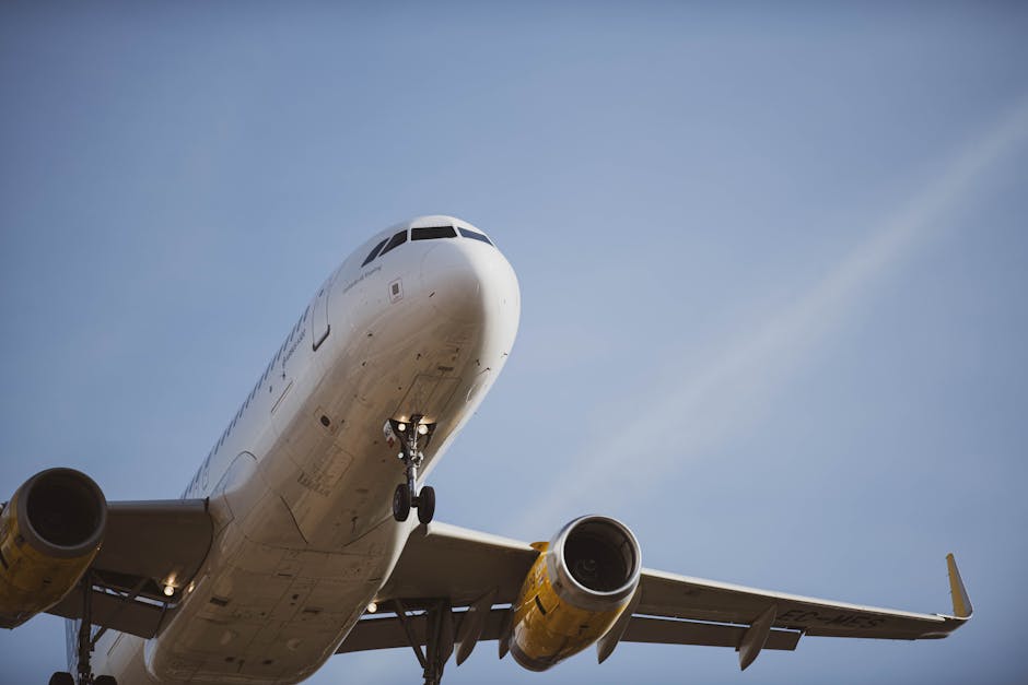 A passenger airplane flying overhead against a clear blue sky, captured from below during landing.