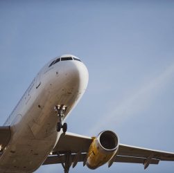 A passenger airplane flying overhead against a clear blue sky, captured from below during landing.