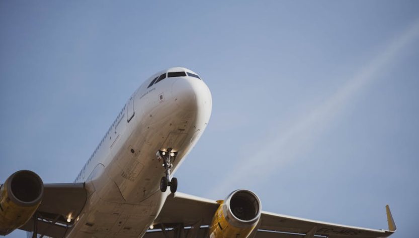 A passenger airplane flying overhead against a clear blue sky, captured from below during landing.