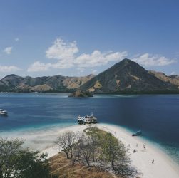 Stunning aerial view of Komodo Island's coastline with turquoise waters and distant mountains under a clear blue sky.