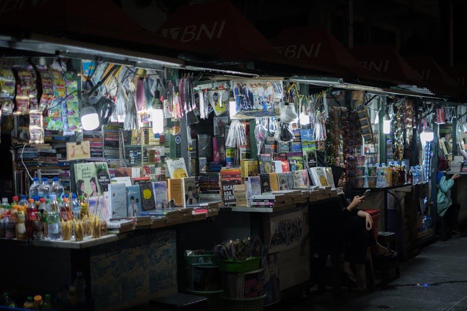 Bustling street market at night featuring book and snack stalls, vibrant atmosphere.