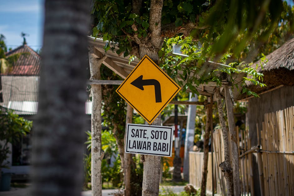 A yellow bend road sign with a local food advertisement in an Indonesian town.