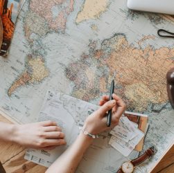 Top view of a woman's hands planning a trip with a map, camera, and travel items.