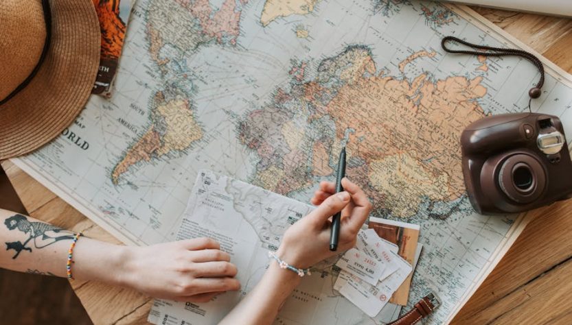 Top view of a woman's hands planning a trip with a map, camera, and travel items.
