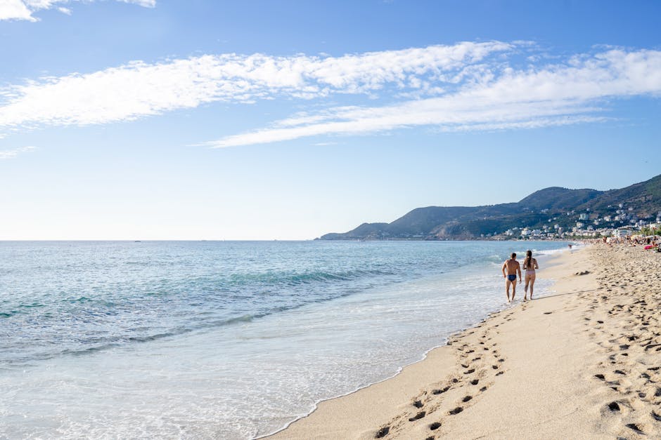 Back view of unrecognizable sportive distant couple running on seashore along rippling sea in tropical resort on sunny summer day